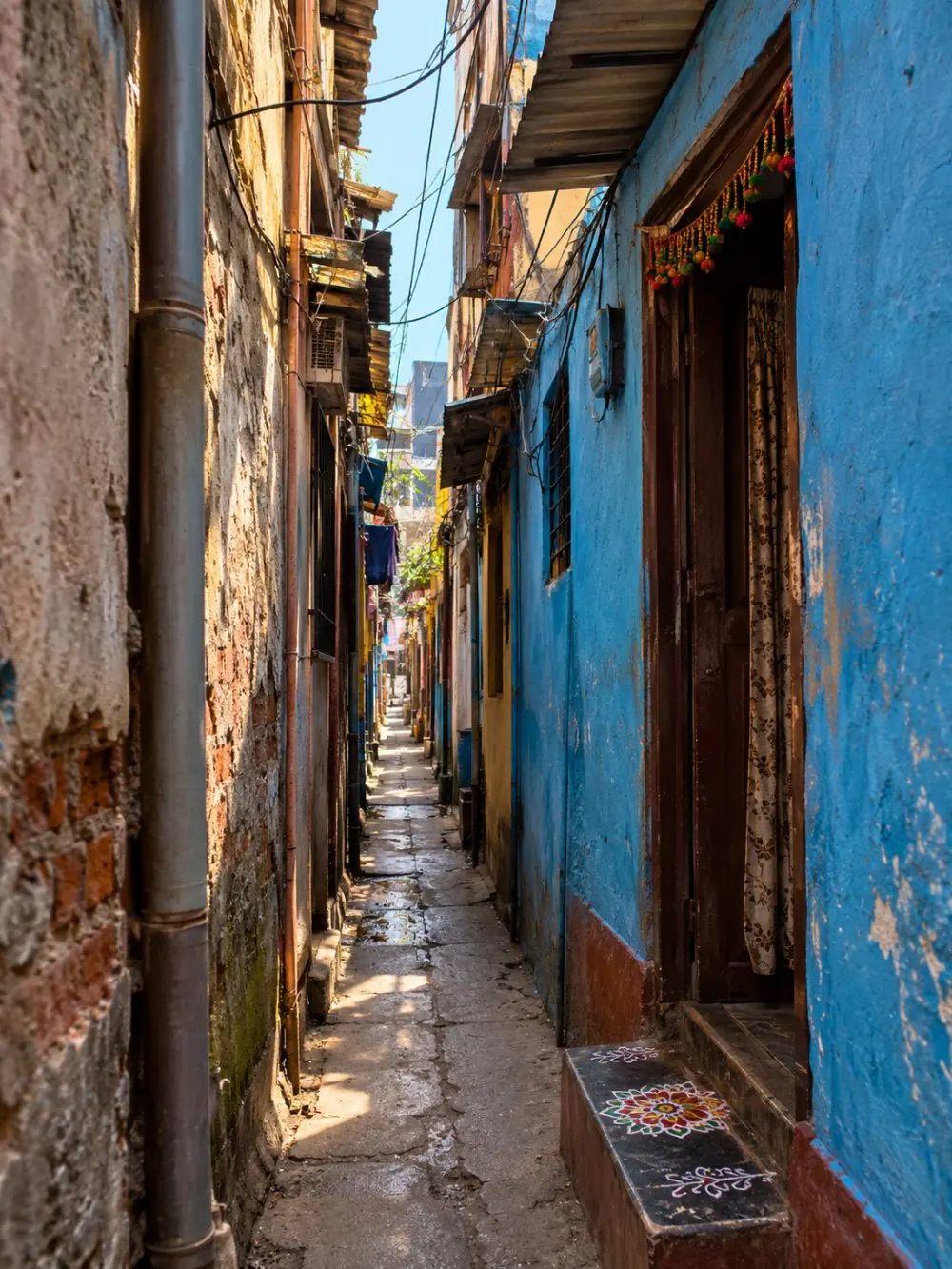 A narrow residential lane with a painted doorway and rangoli on the step